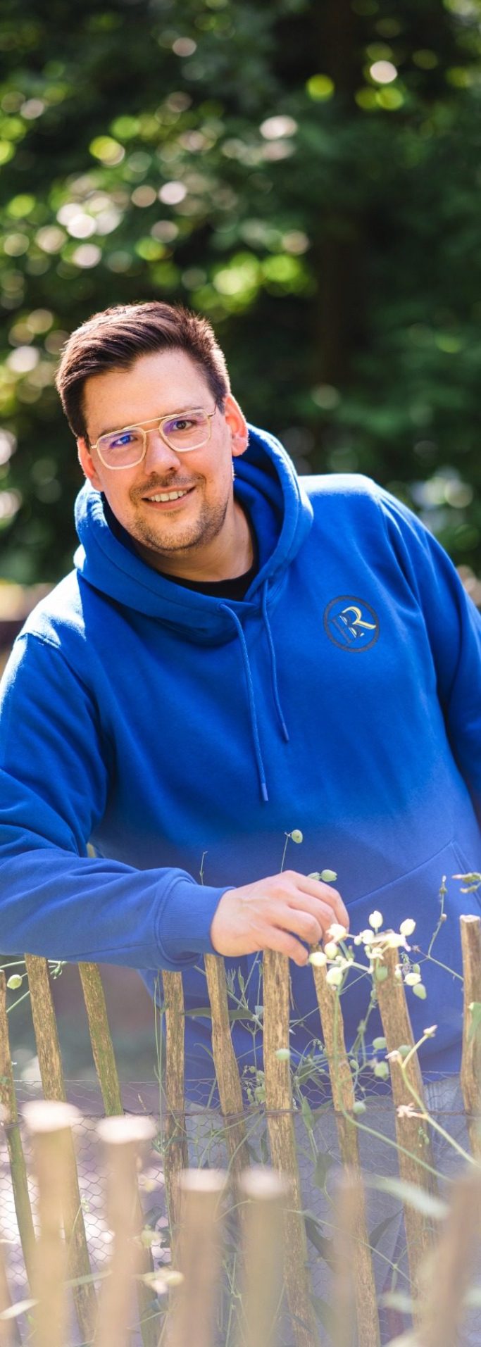 Lächelnder Mann in beiger Jacke sitzt auf einer Treppe im Freien.