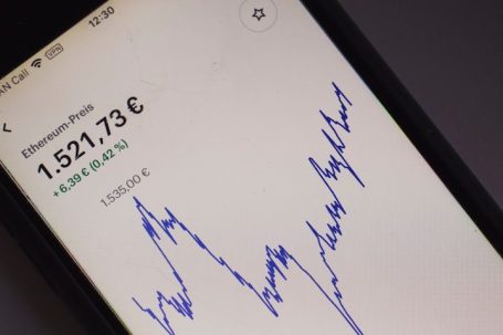 Zwei Männer in Anzügen besprechen einen Bericht und schauen auf ein Smartphone.